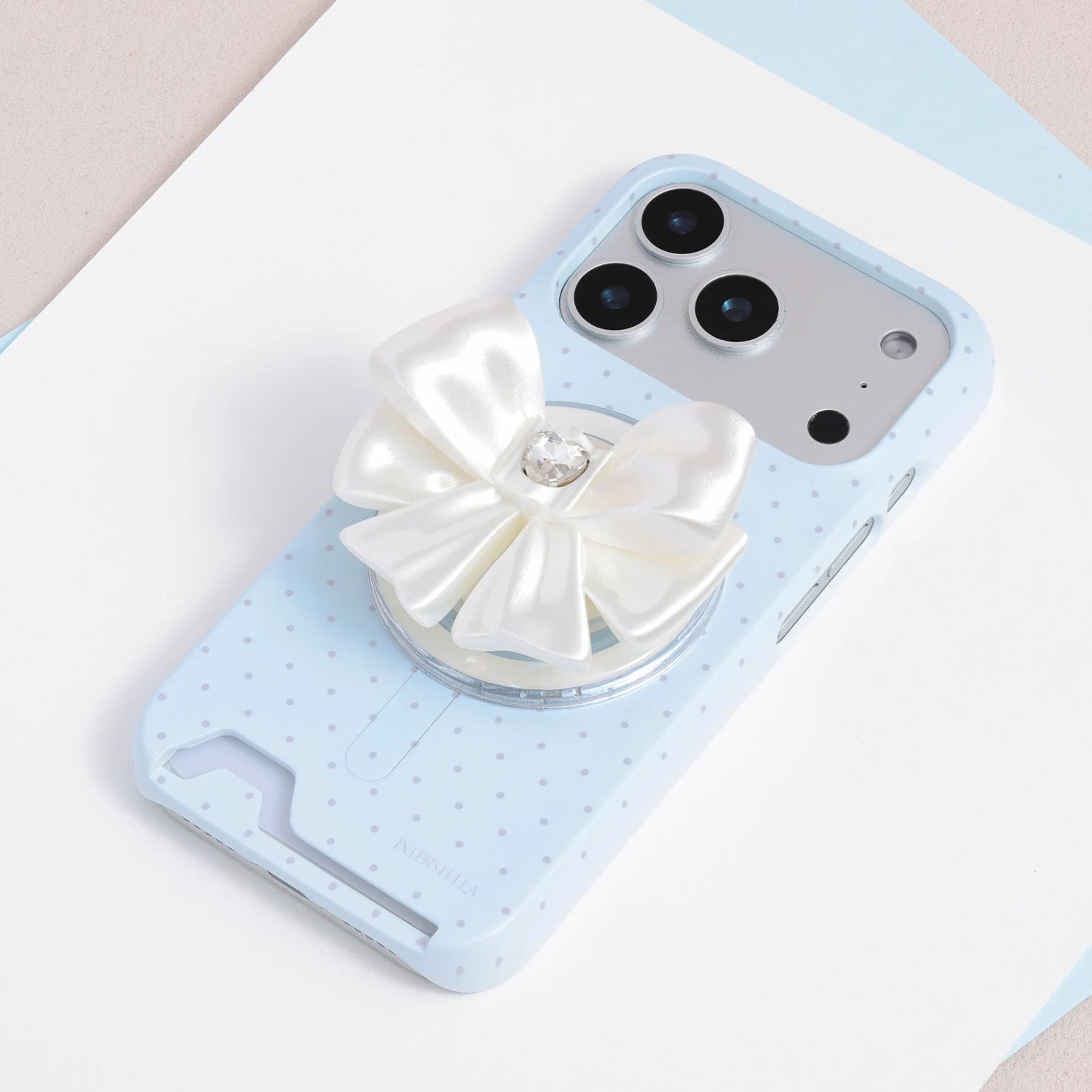 Ivory white jewel bow phone grip stand attached to a pale blue micro polka dot phone case.