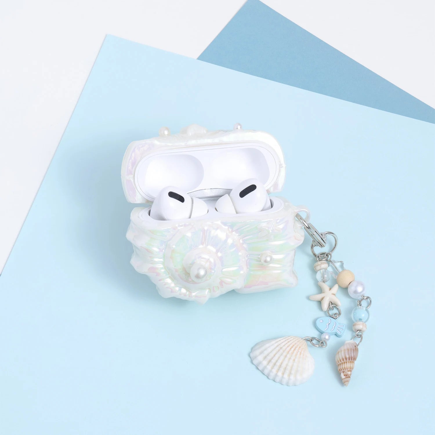 Open pearl-white conch AirPods case with white AirPods inside, featuring an iridescent finish and a decorative marine charm chain.