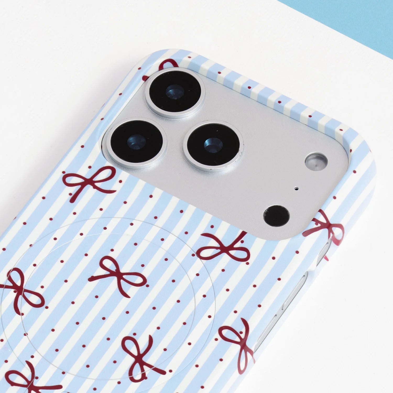 Close-up of the striped ribbon bow phone case camera area showing powder-blue stripes, crimson bows, and smooth PC finish.