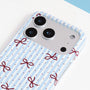 Close-up of the striped ribbon bow phone case camera area showing powder-blue stripes, crimson bows, and smooth PC finish.