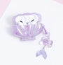 Open lilac shell-shaped AirPods case with white AirPods inside, featuring an iridescent finish and a dangling translucent mermaid-tail charm.