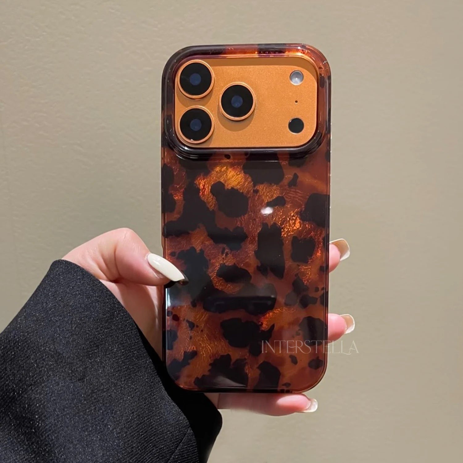 Front-facing hand-held view of a tortoiseshell leopard phone case with oversized spots and structured camera frame