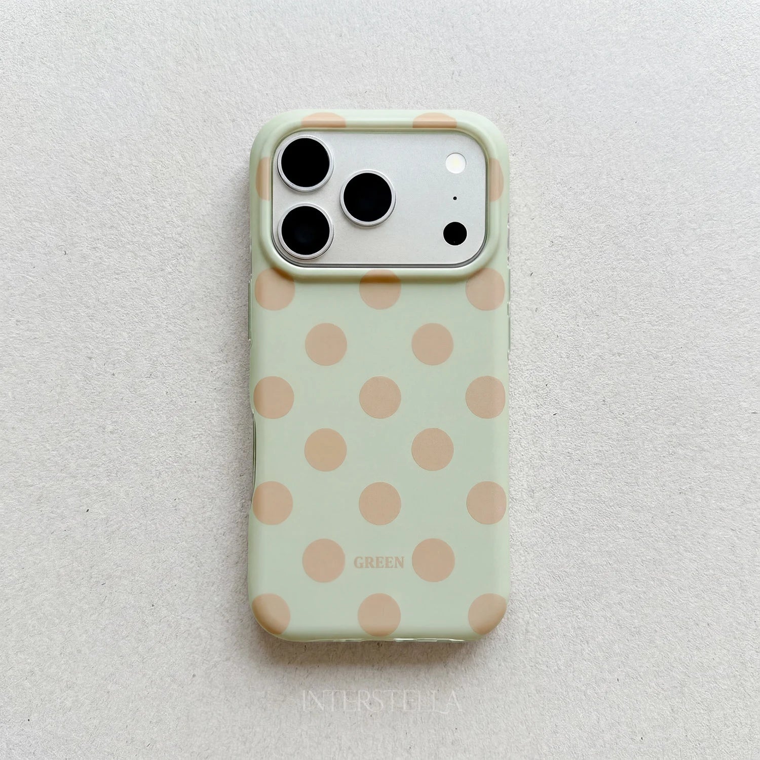Soft mint green polka dot phone case with warm beige dots and raised camera surround on a light neutral background.