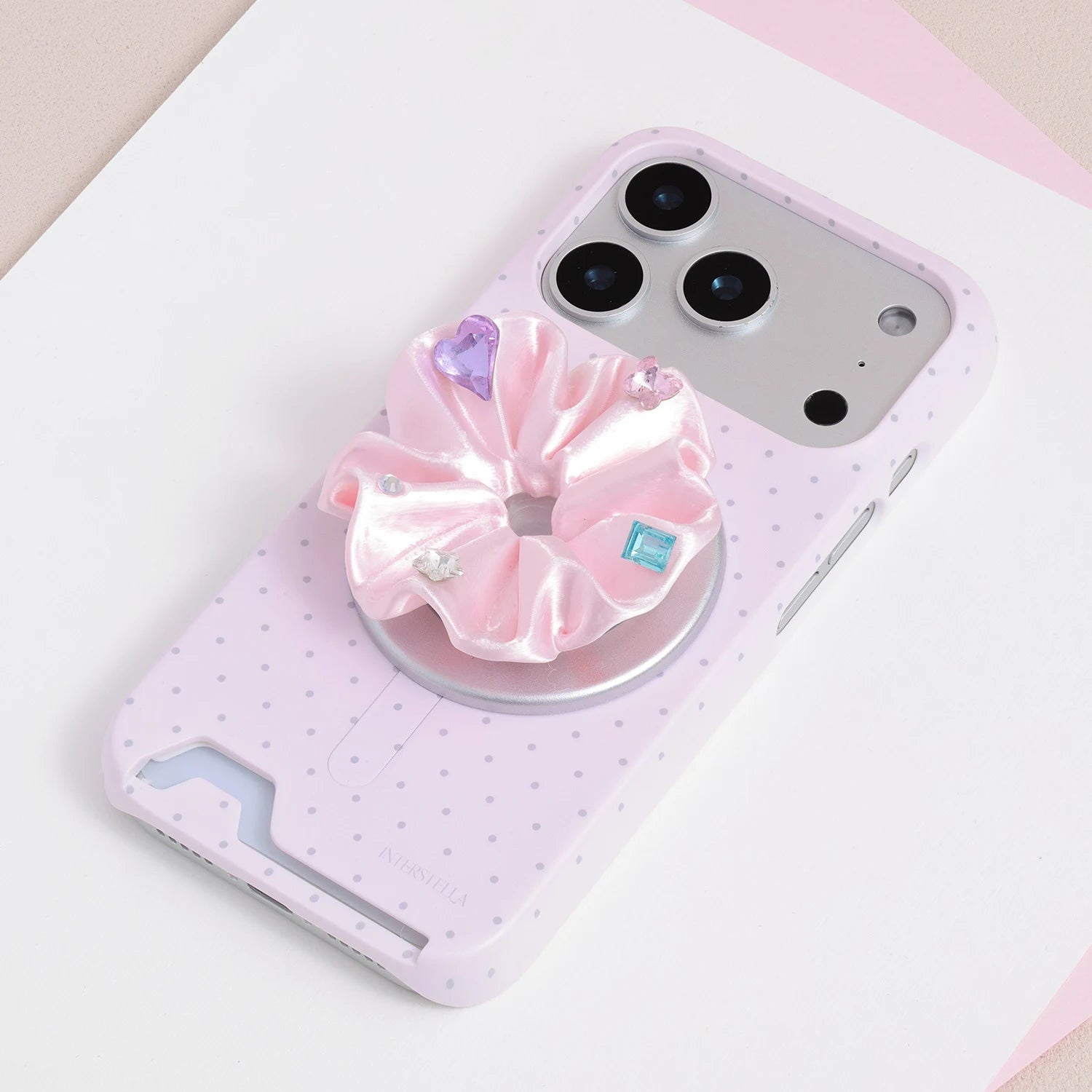 Pink jewel rosette phone grip stand mounted on a pale pink micro polka dot card-slot phone case.