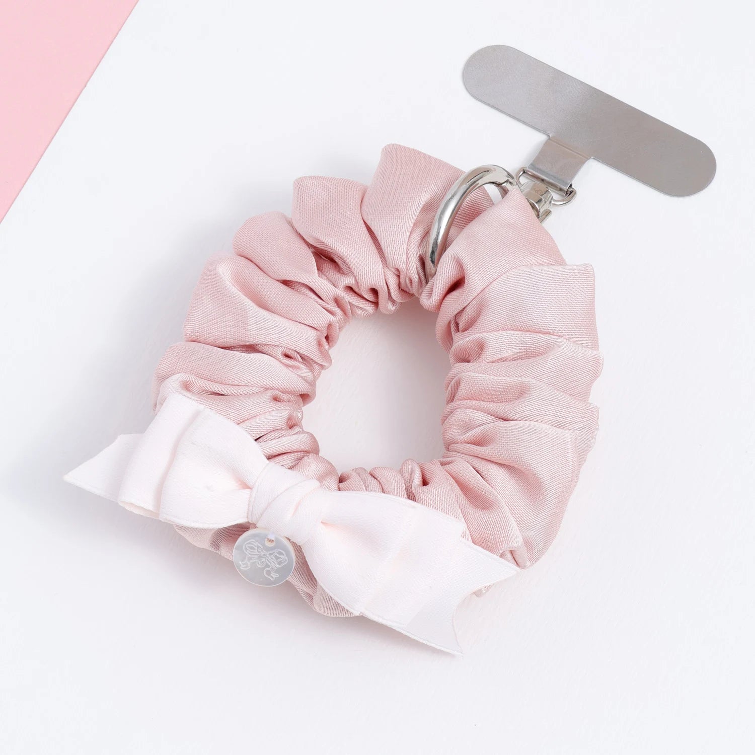 Blush pink fabric phone hanging ring shown flat with metal attachment tab, soft gathered folds, and an ivory bow accent.