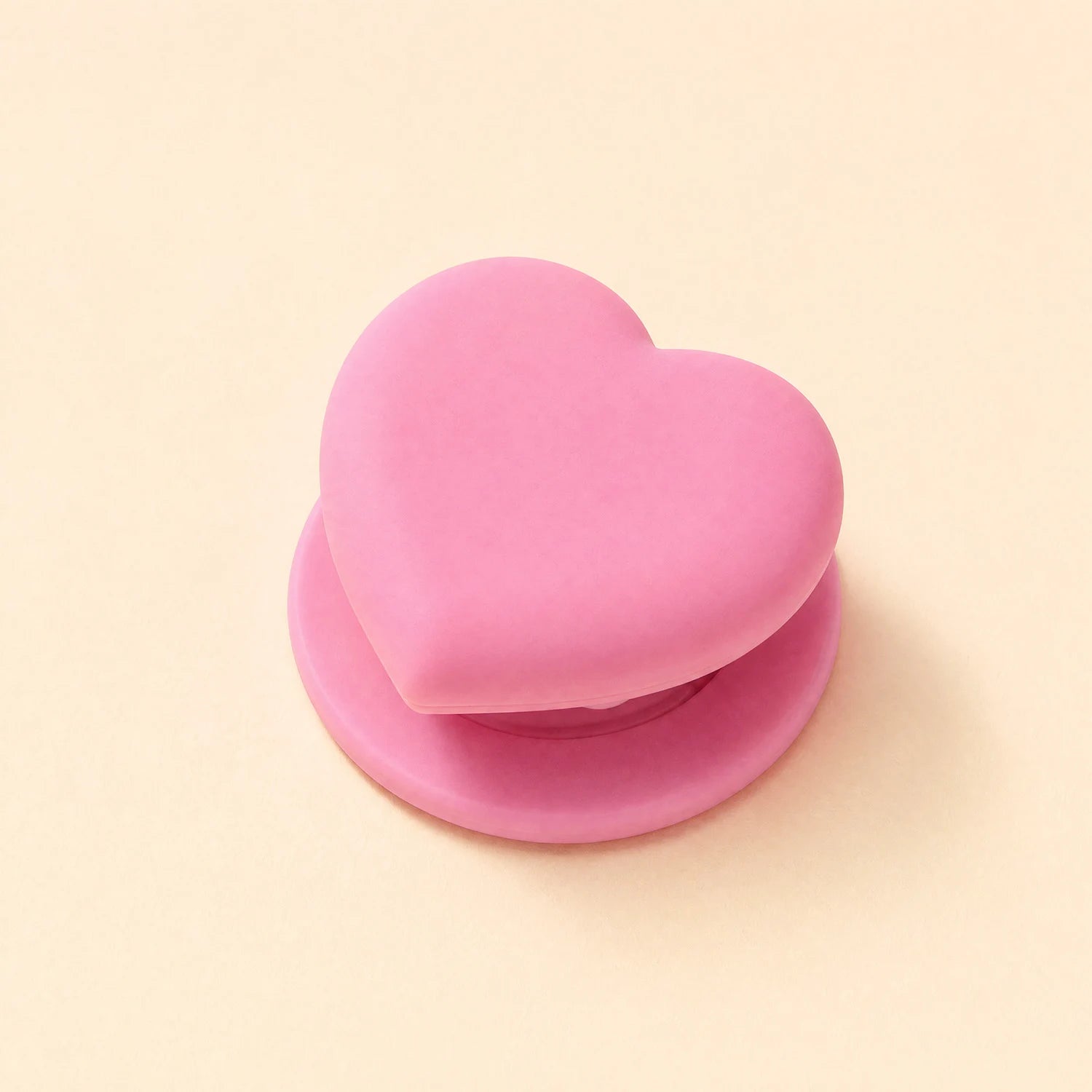 Blush pink heart phone grip stand with a matching pink round base displayed on a beige background.