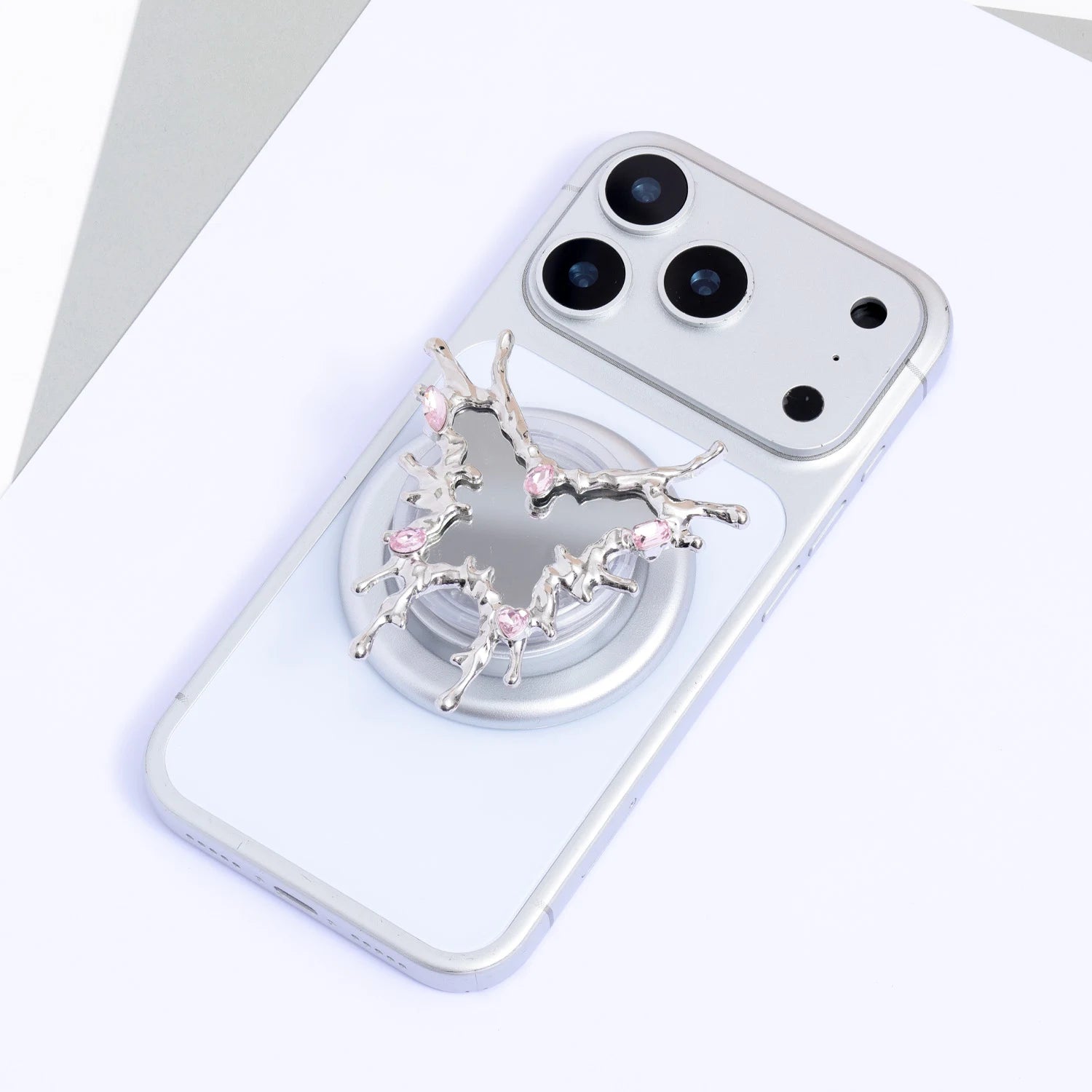 Cross-like silver-tone mirror phone stand with branching sculptural edges and pink crystal accents attached to a silver phone.