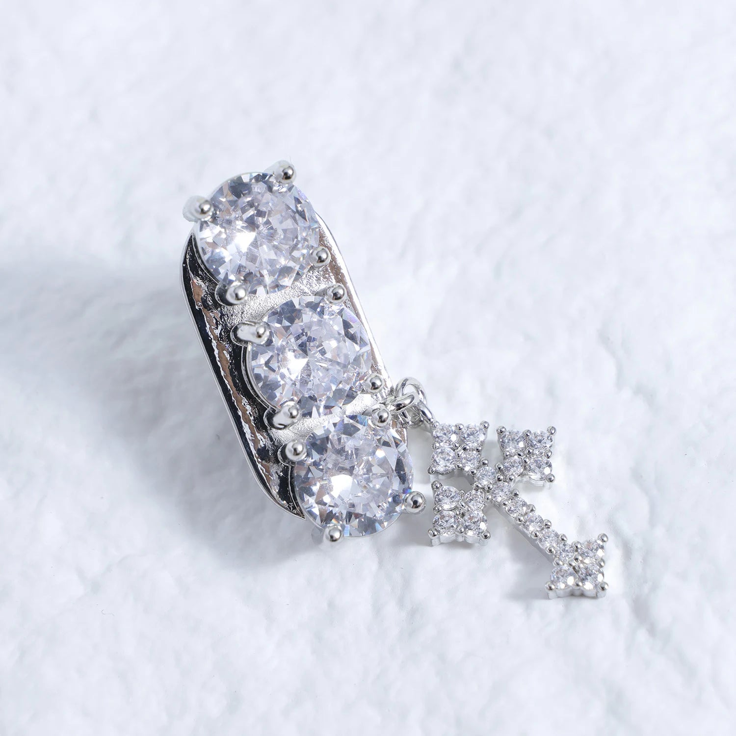 Silver-tone crystal ear charm with clear stones and dangling cross detail on a white textured background