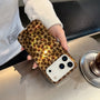 Lifestyle image of a woman holding a petite leopard phone case beside an iced coffee, paired with tortoiseshell glasses for a refined vintage-inspired look.