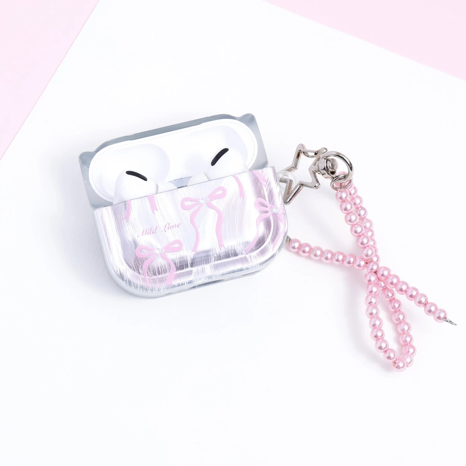 Front view of a pearly silver AirPods case decorated with pink ribbon illustrations and a glossy pink pearl-bead bow charm attached with a metal clasp.