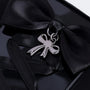 Close-up of a black phone case with a handmade satin bow, polished silver pendant charm, and corset-style ribbon detailing.