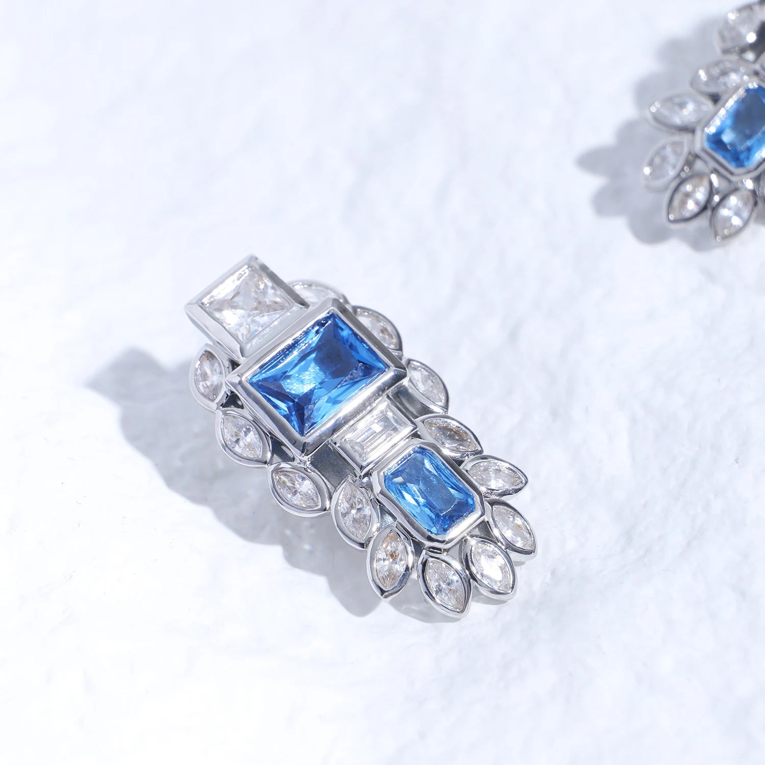 Blue gemstone ear charm with Swarovski crystal accents and silver-tone plated reliquary silhouette on a white textured surface