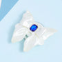 Angled close-up of an ivory bow-shaped phone stand showing the dimensional ribbon form and embedded sapphire-blue jewel detail.