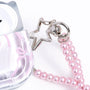 Close-up detail of the side charm on a silver ribbon-print AirPods case, showing the polished metal hardware and pink pearl-bead bow-shaped accessory.