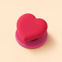 Rose pink heart phone grip stand with a deeper pink round base displayed on a beige background.