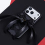 Full view of a matte black phone case with a large black satin bow and glossy black bell charm, styled against a black and red backdrop.