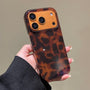 Hand holding a glossy tortoiseshell leopard phone case with oversized dark spots and raised camera surround