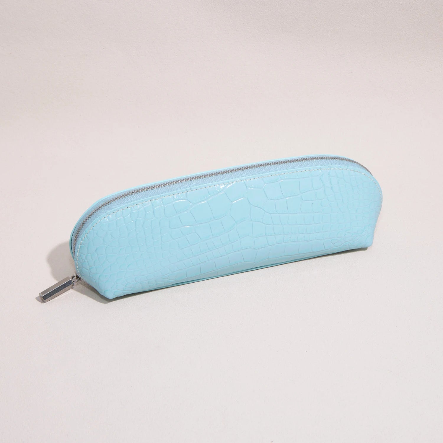 Close-up of the croc-embossed leather texture and silver-tone zipper on a slim pencil case