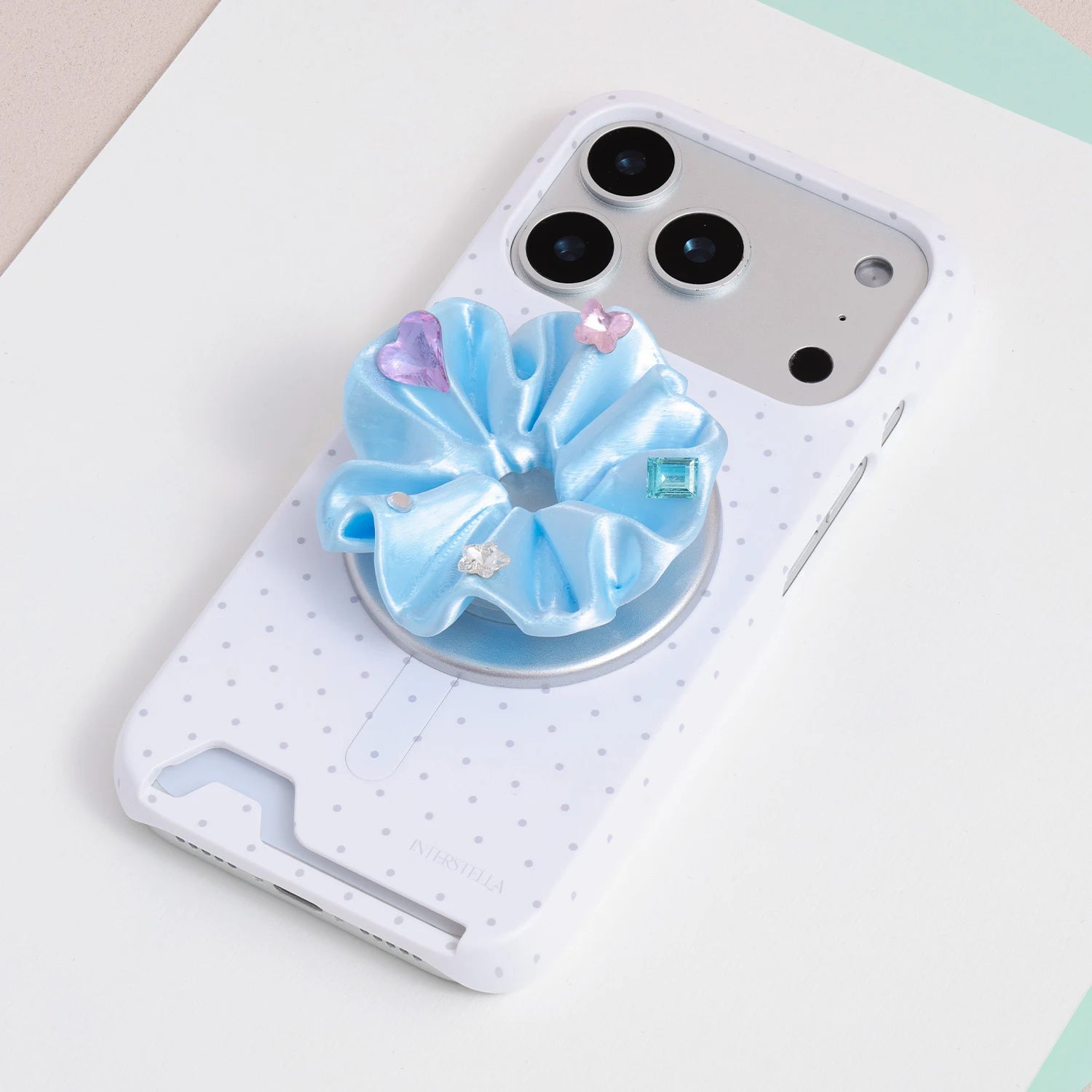 Blue jewel rosette phone grip stand mounted on a white micro polka dot card-slot phone case.