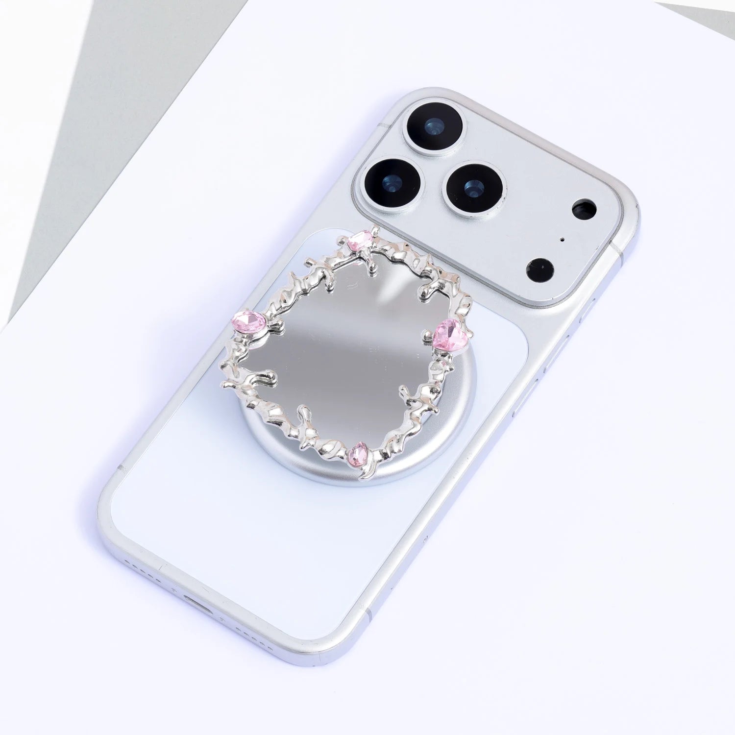 Ornamental frame-style silver-tone mirror phone stand with pink crystal accents mounted on a silver phone with a circular base.