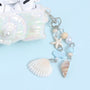 Detail of the dangling ocean charm chain attached to the conch AirPods case, featuring shell pendants, beads, a small starfish, and soft sea-inspired pastel accents.