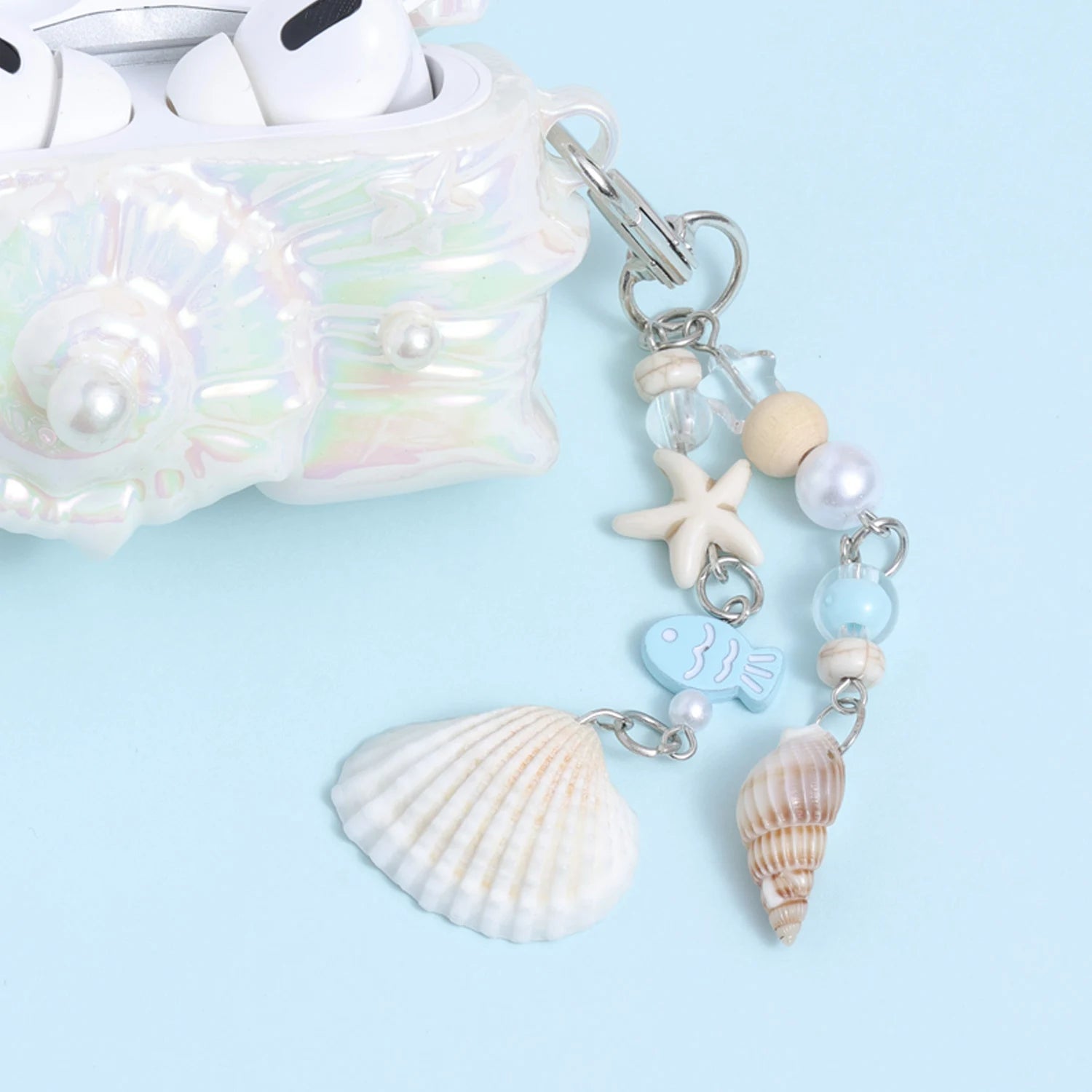 Detail of the dangling ocean charm chain attached to the conch AirPods case, featuring shell pendants, beads, a small starfish, and soft sea-inspired pastel accents.