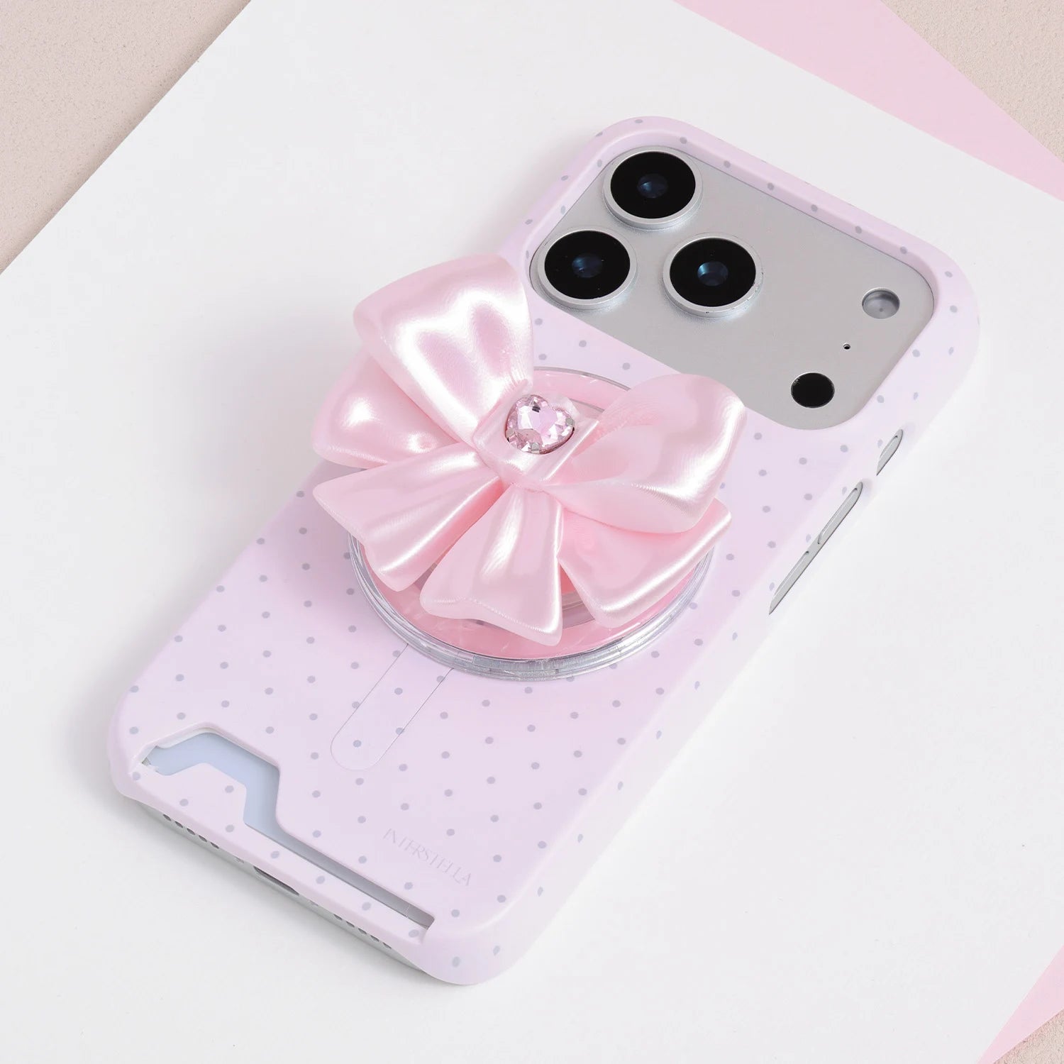 Blush pink jewel bow phone grip stand attached to a soft pink micro polka dot phone case.