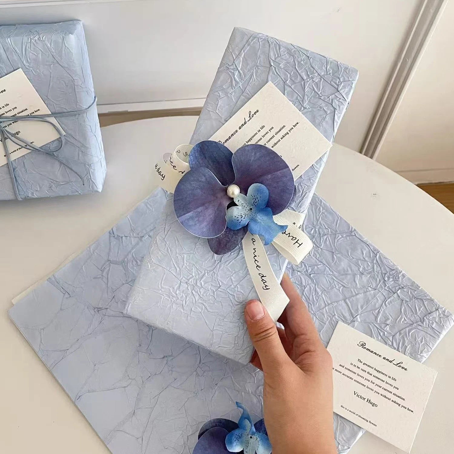 Ciel d’Orchidée gift wrapping presentation with blue orchid detail, textured paper, and romantic ribbon finish