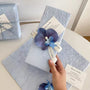 Ciel d’Orchidée gift wrapping presentation with blue orchid detail, textured paper, and romantic ribbon finish