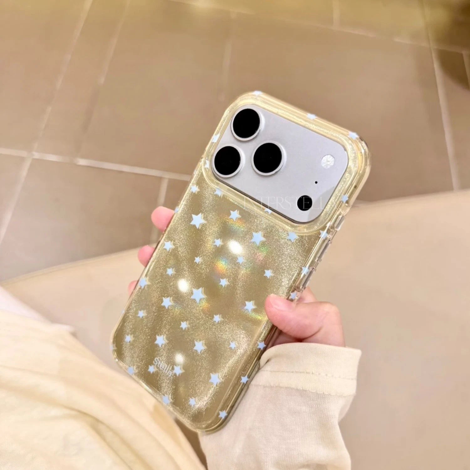Hand holding a gold shimmering star phone case with pale blue stars and clear edges