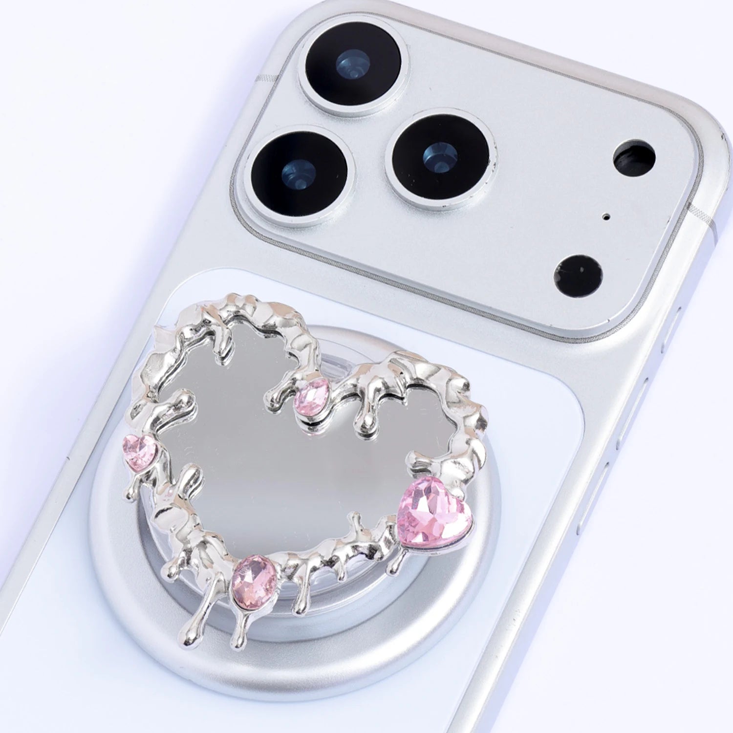Close-up of the Heart Reliquary phone stand showing the reflective mirrored center, sculptural silver-toned edge, and soft pink crystal details.