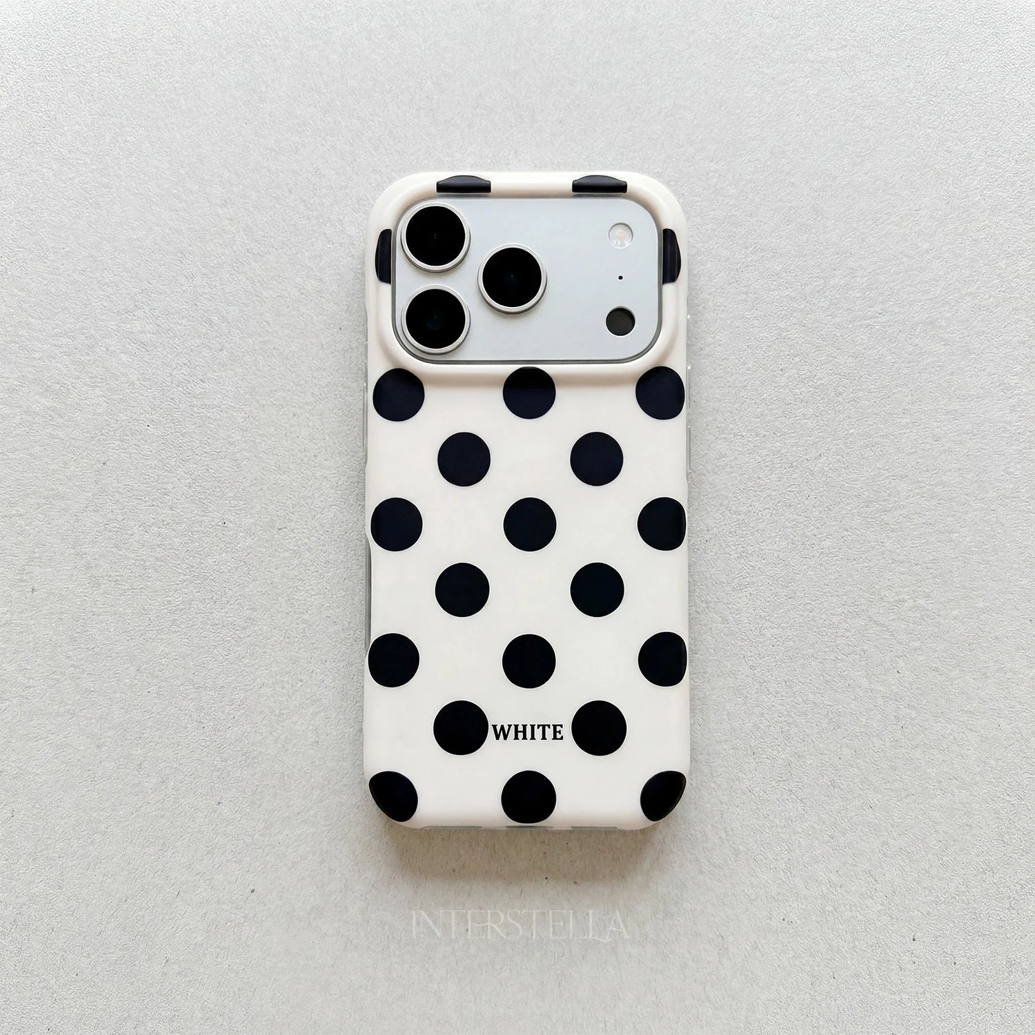 Ivory white polka dot phone case with bold black dots and raised camera surround on a light neutral background.