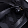 Detailed close-up of a black satin bow and glossy black bell charm on a matte black phone case with ribbon styling across the back.