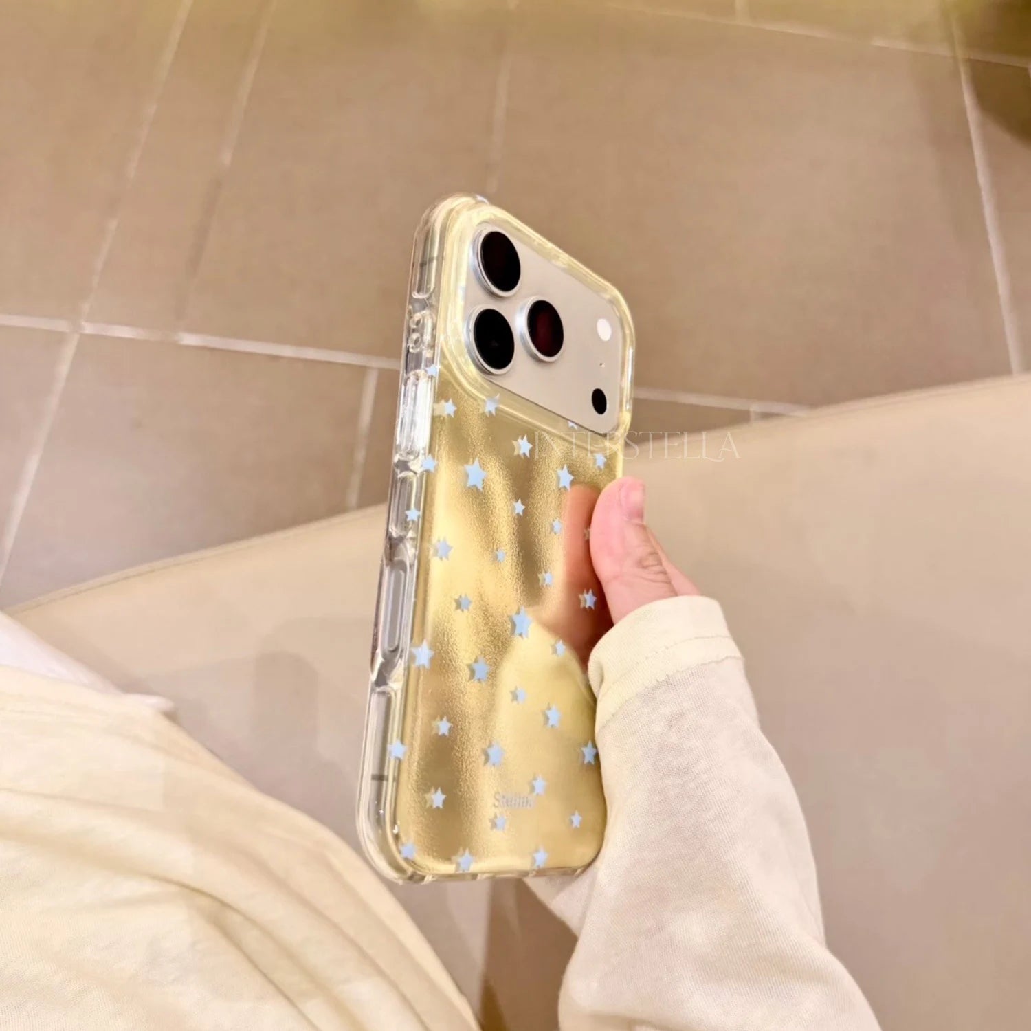 Side view of a gold shimmering star phone case with pale blue stars held in hand