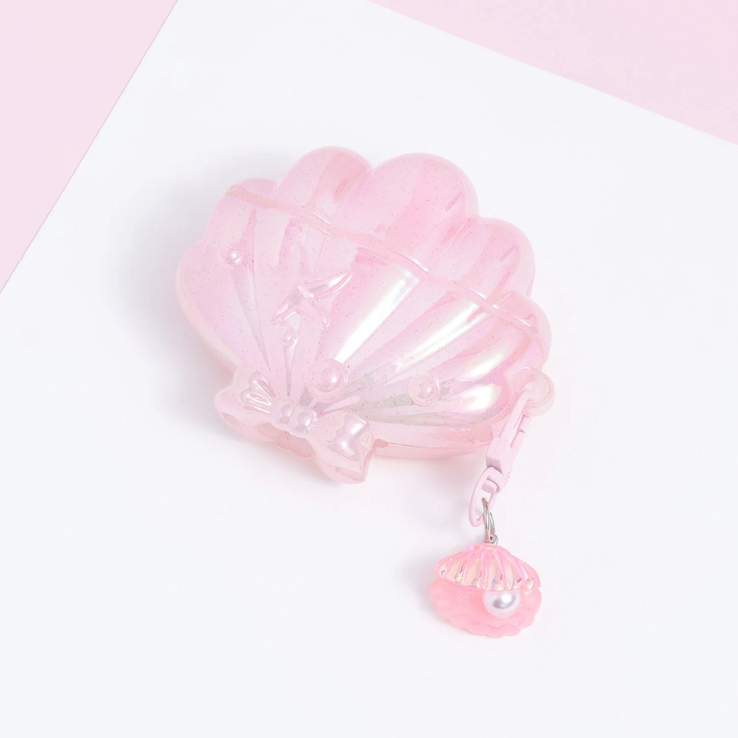 Closed pink shell AirPods case with a glossy blush iridescent finish and a dangling miniature shell-and-pearl charm.