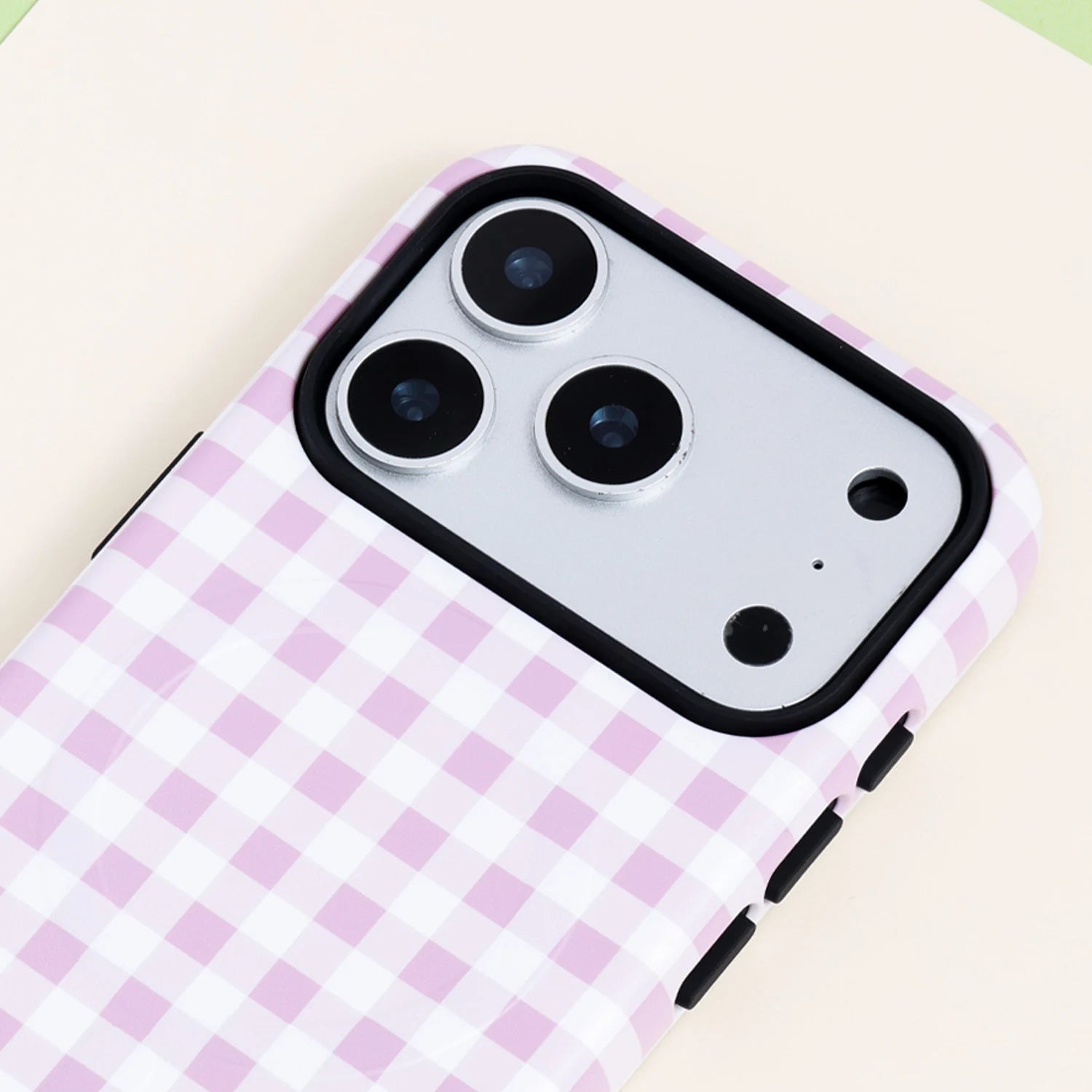 Close-up of the Blush gingham phone case highlighting the soft pink check design, polished outer shell, and protective black camera surround.