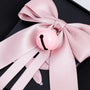 Detailed close-up of a blush pink satin bow and matching bell charm on a matte black phone case.