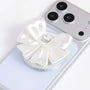 Close-up of an ivory white 3D-printed jewel bow phone grip stand with glossy satin-like folds and a crystal-inspired center on a silver phone.