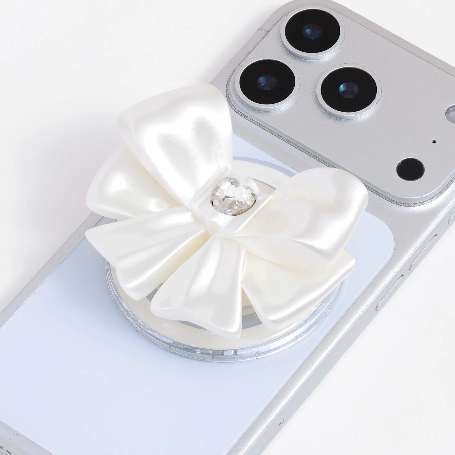 Close-up of an ivory white 3D-printed jewel bow phone grip stand with glossy satin-like folds and a crystal-inspired center on a silver phone.