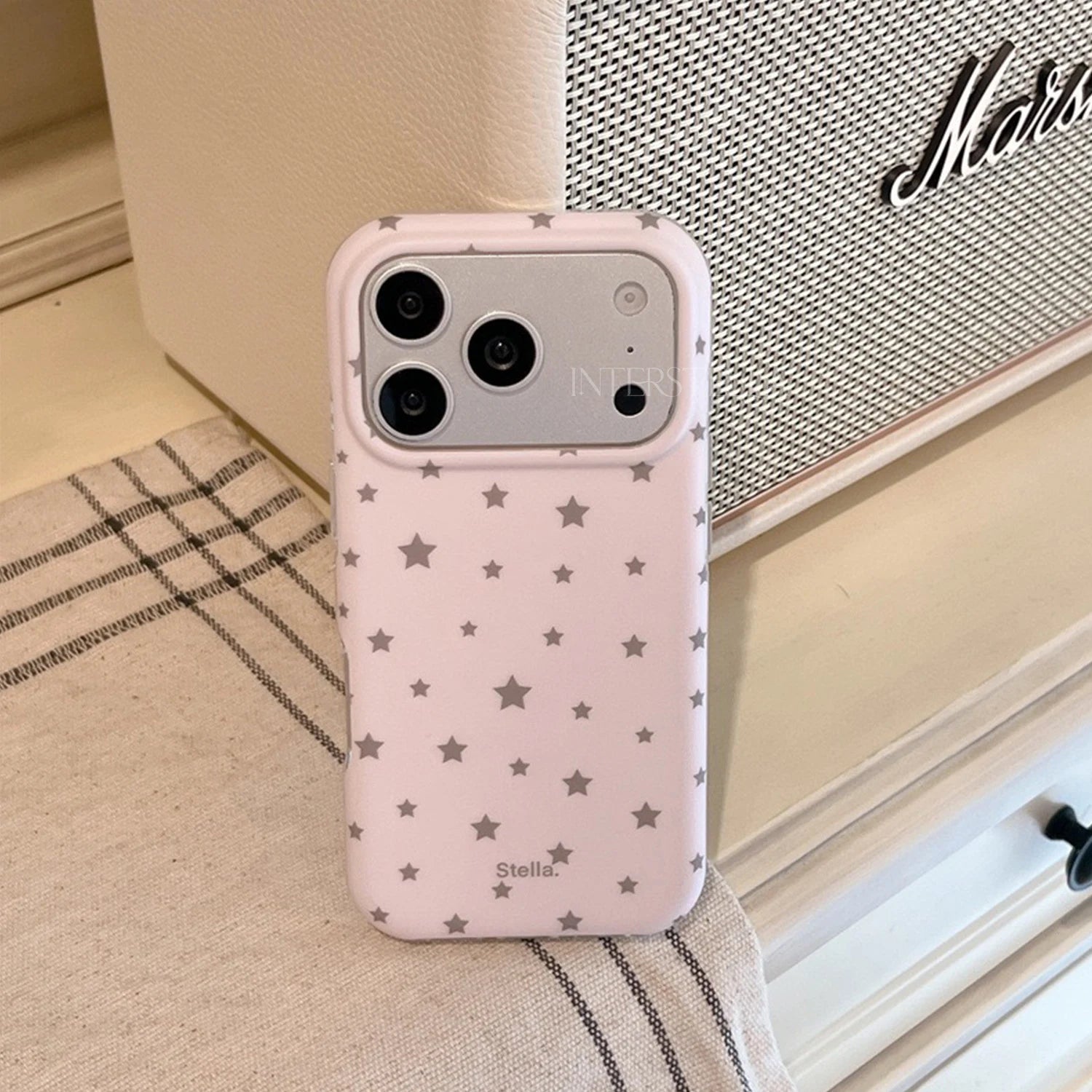 Blush pink matte star phone case with silver star print displayed beside a speaker