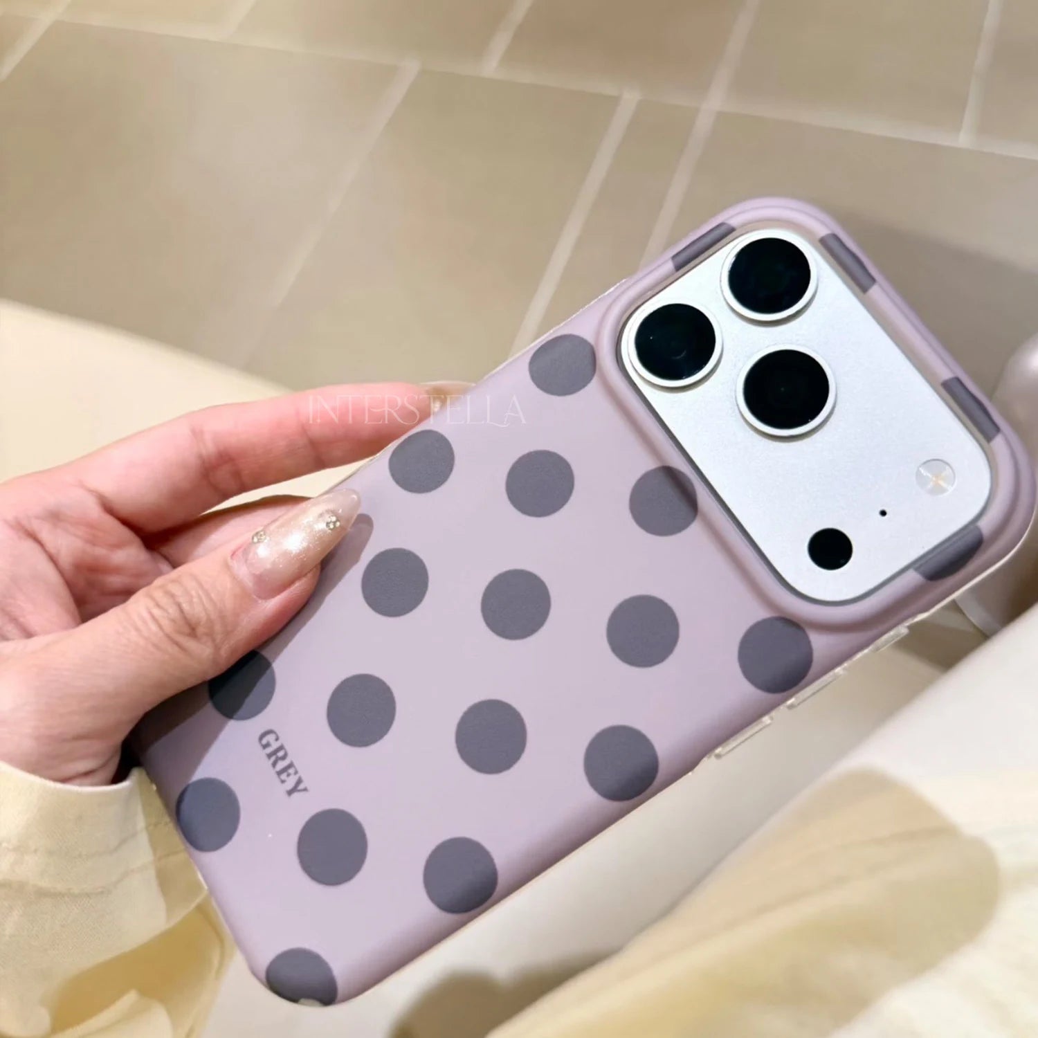 Angled close-up of a lilac polka dot phone case with charcoal grey dots, showing the smooth finish and raised camera surround.