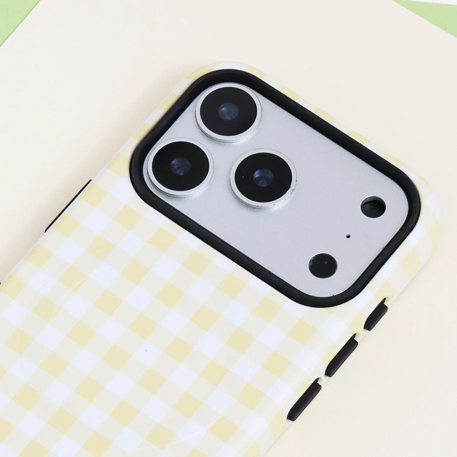 Close-up of the Buttercream gingham phone case featuring the pale yellow check pattern, smooth structured surface, and raised black camera frame.