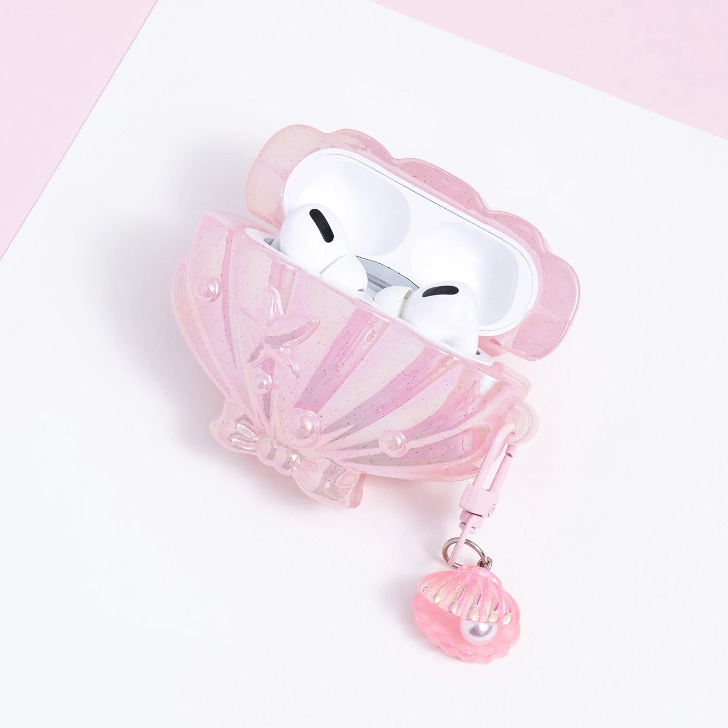 Open pink shell-shaped AirPods case with white AirPods inside, featuring pearl accents, a starfish motif, and a dangling shell pearl charm.