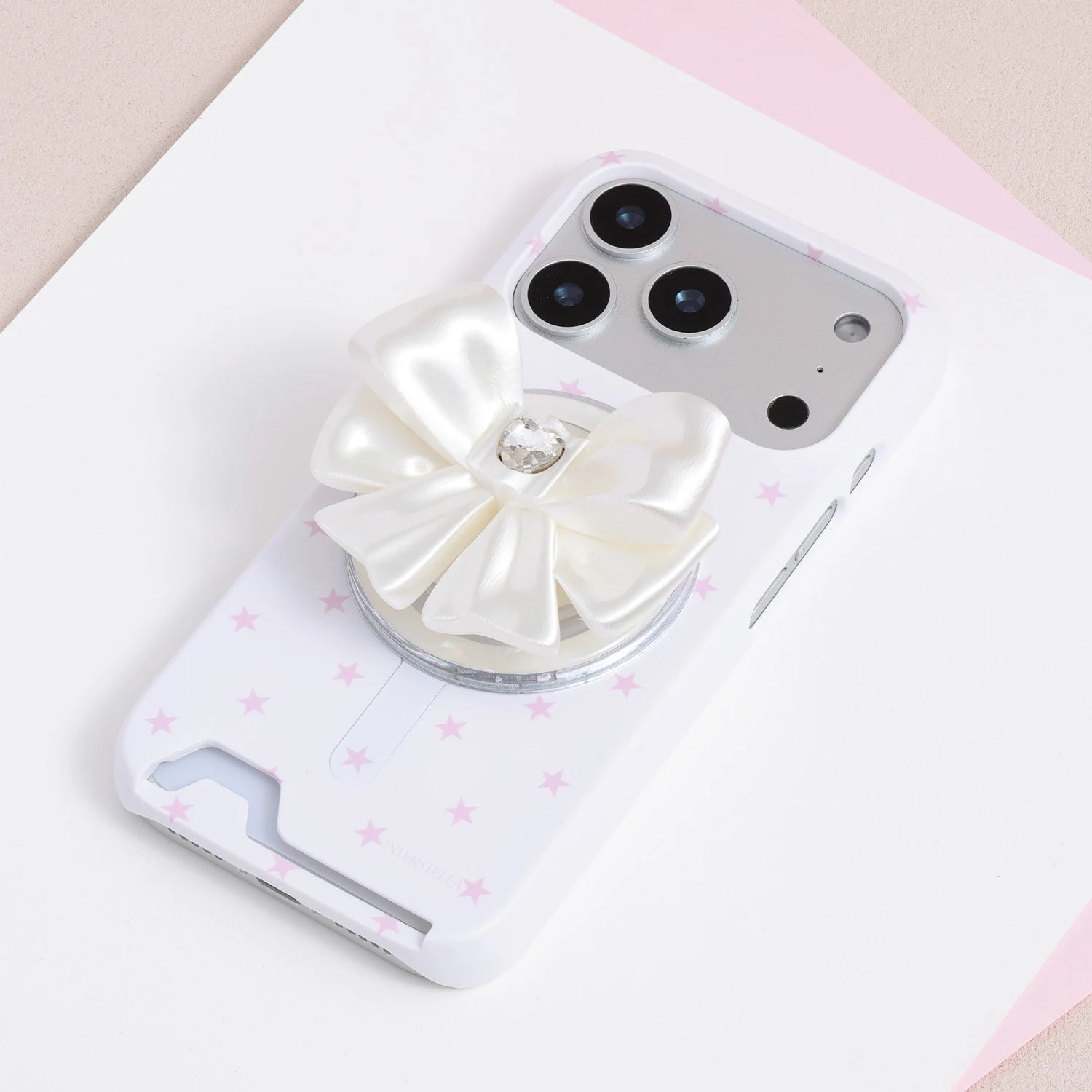 Ivory white jewel bow phone grip stand mounted on a white phone case with soft pink star print.