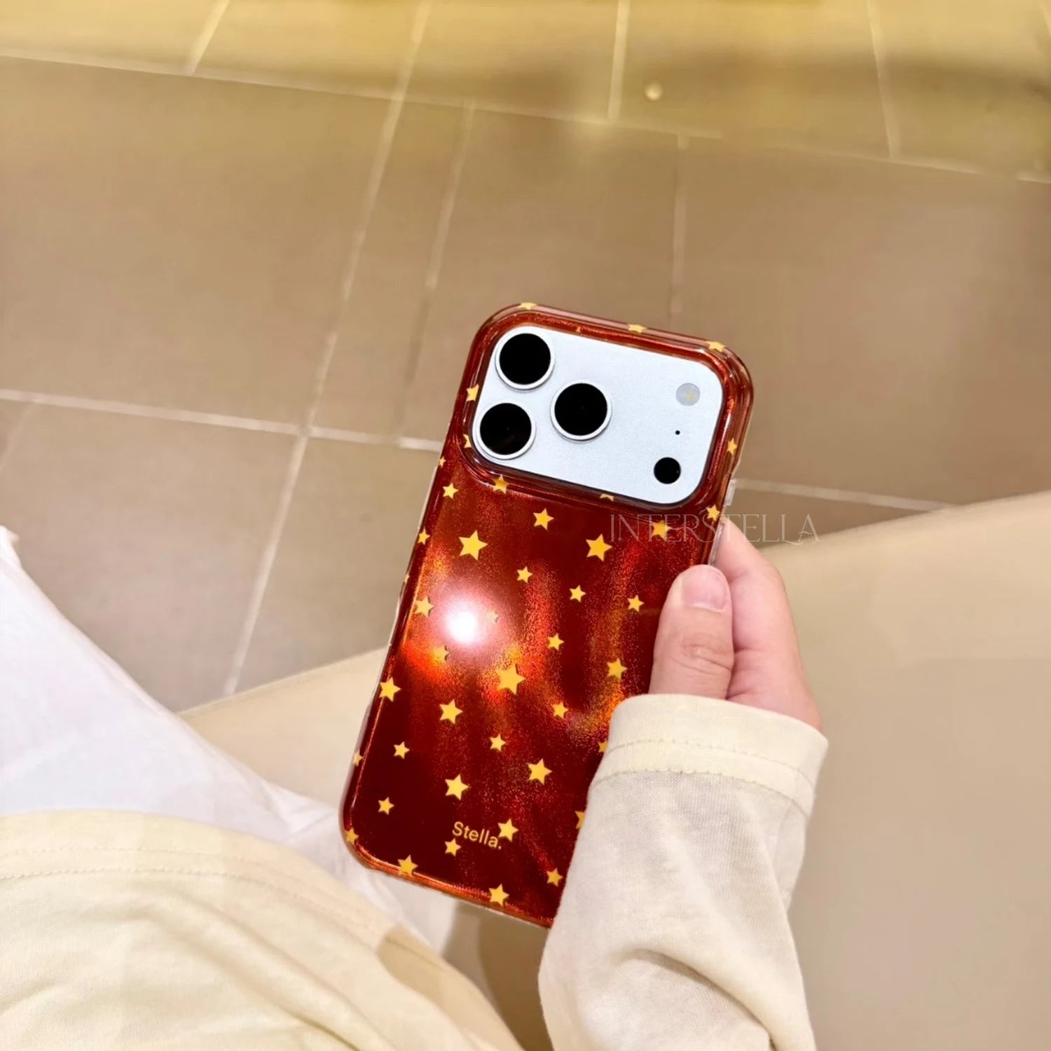 Hand holding a deep red shimmering star phone case with gold stars and glossy finish