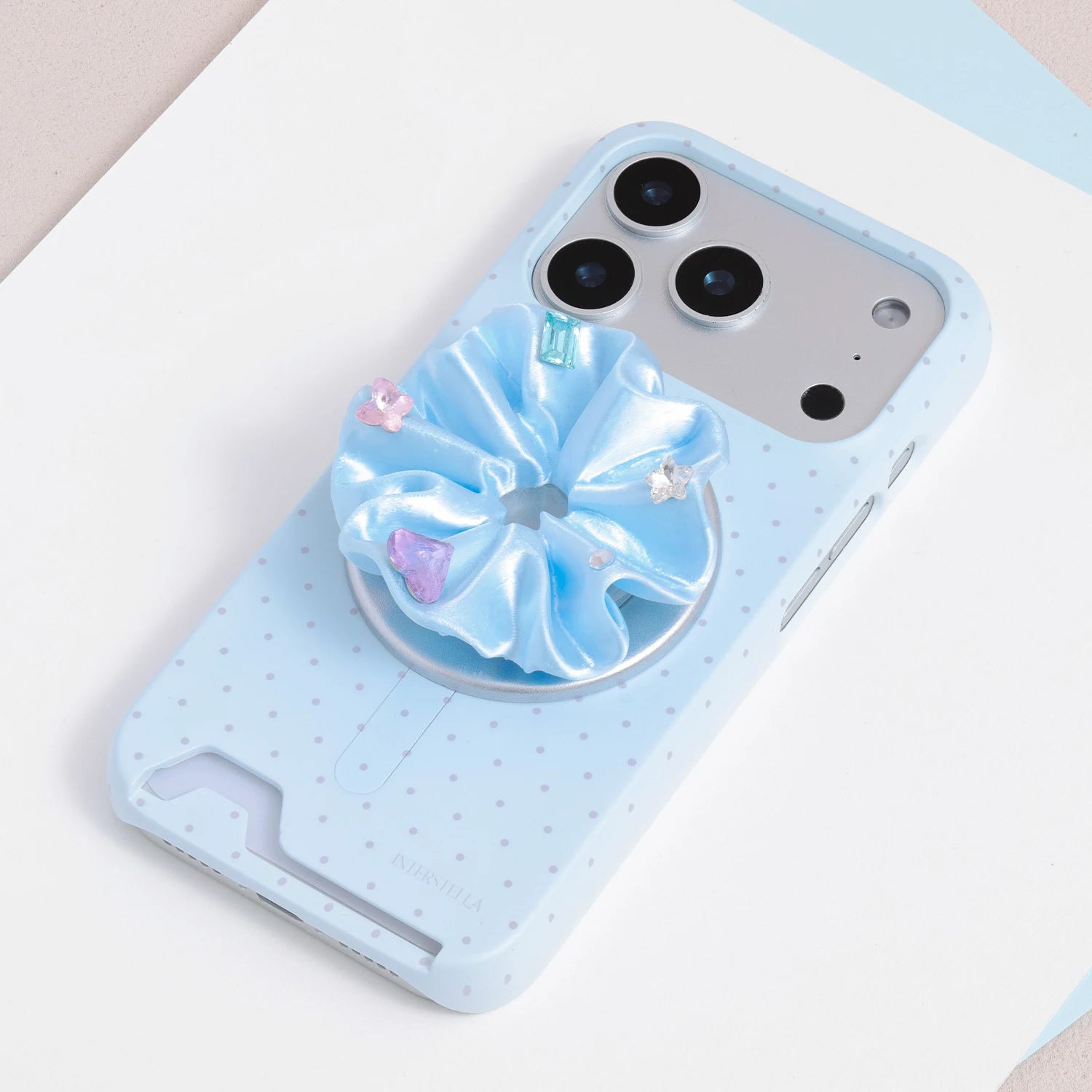 Blue jewel rosette phone grip stand attached to a pale blue phone case with fine micro polka dot print.