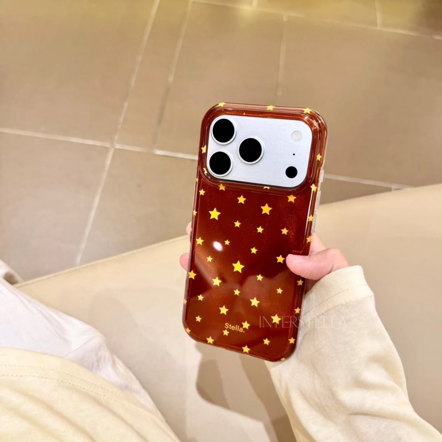 Front view of a deep red shimmering star phone case with gold stars held in hand