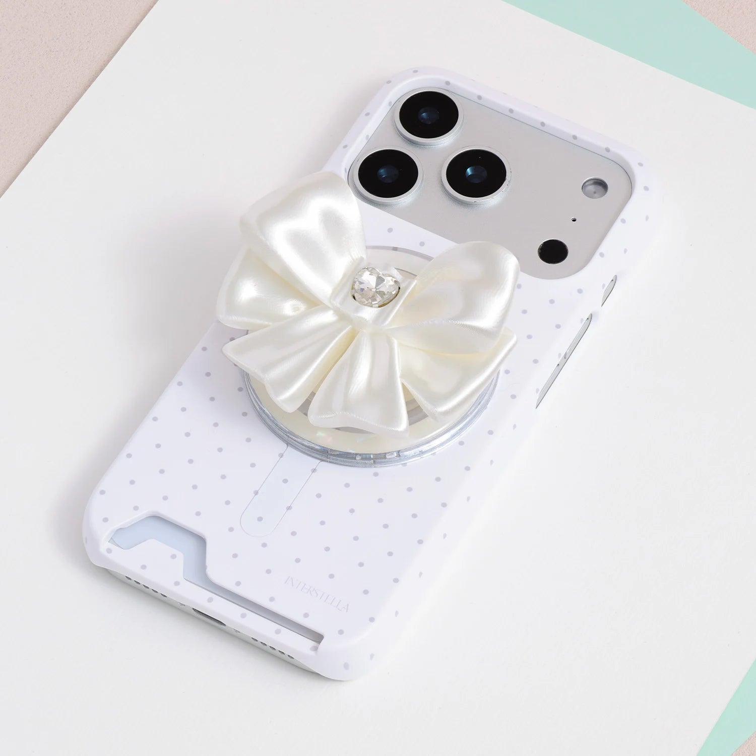 Ivory white jewel bow phone grip stand attached to a white phone case with soft pink polka dots.
