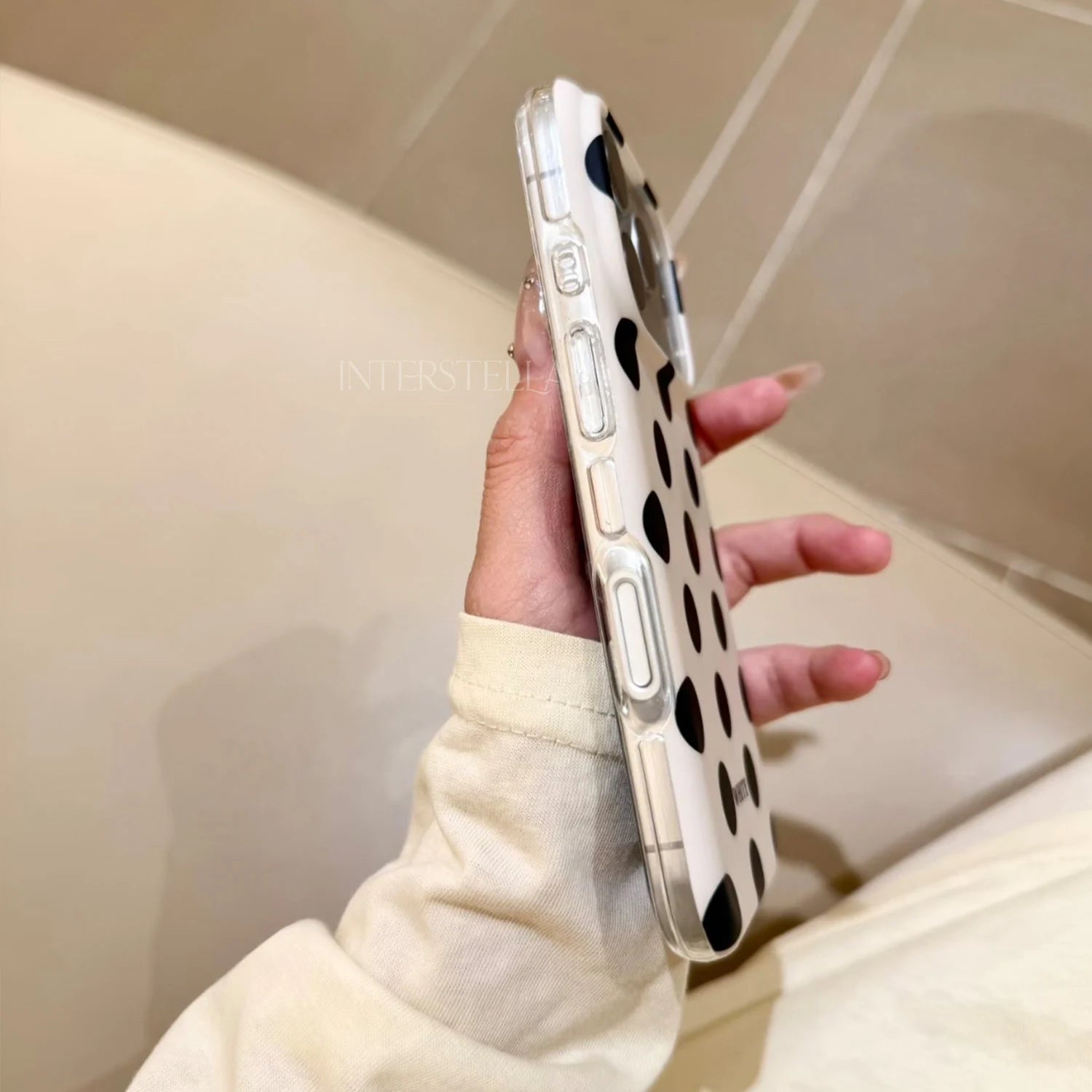 Close side view of an ivory polka dot phone case with bold black dots, showing the clear bumper edge and covered buttons.