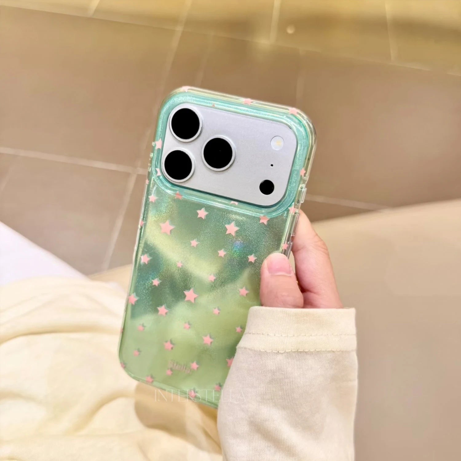Hand holding a mint green shimmering star phone case with pink stars and clear edges